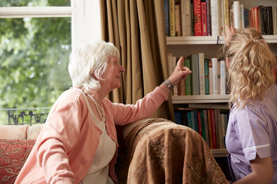 Care worker getting a book for happy elderly woman